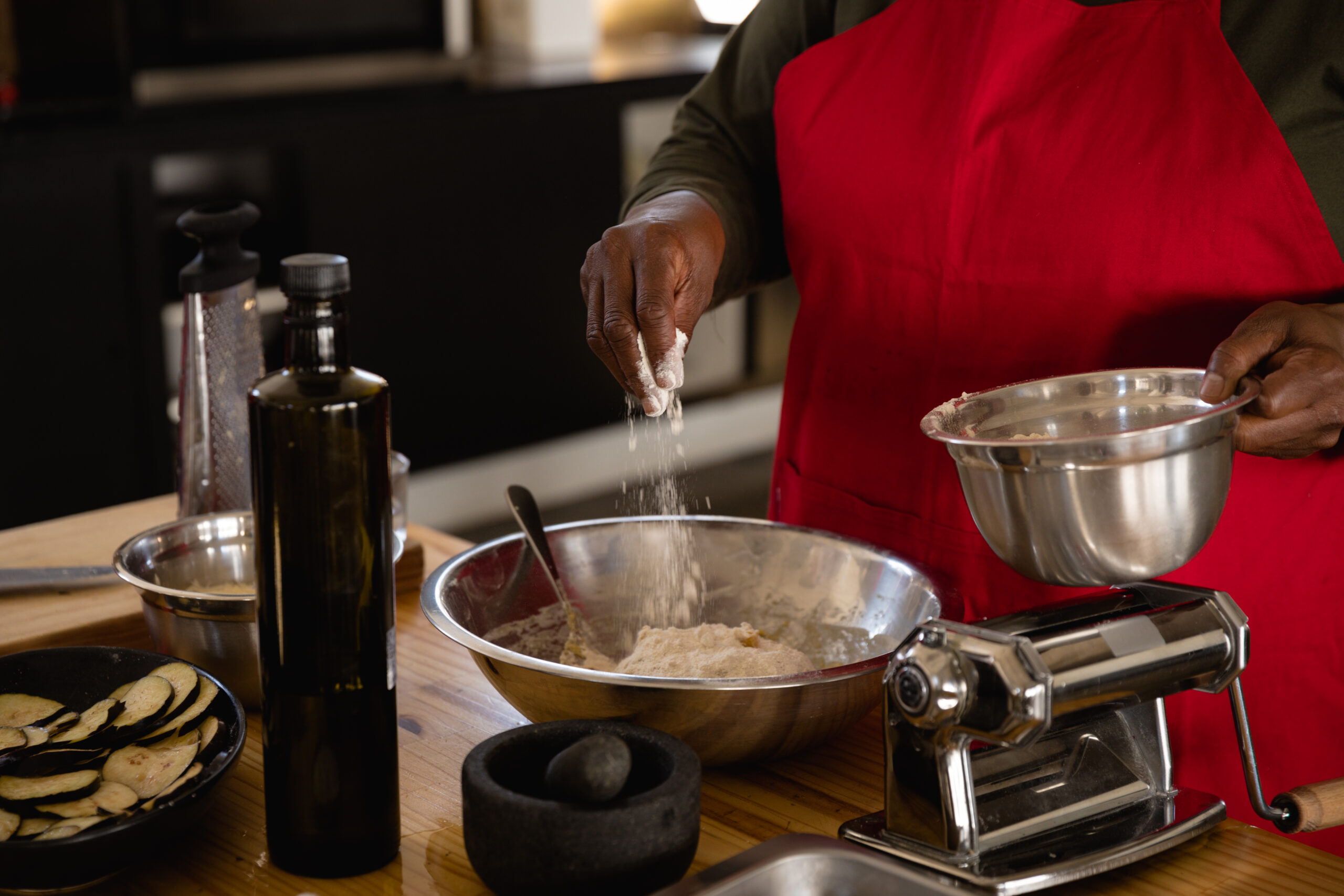 Front view mid section of an Senior African woman wearing a red apron preparing food at a cookery class, adding flour to a mixing bowl nice touch